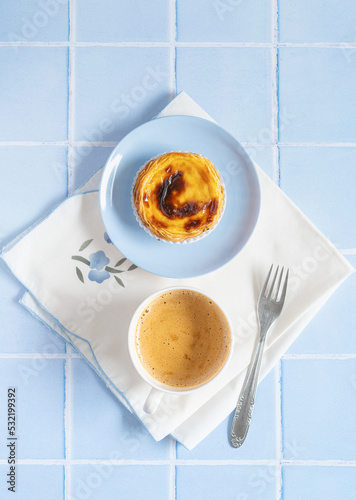 Traditional Portuguese egg tart dessert Pasteis Pastel de nata or Pastels de Belem with a cup of coffee and fork on the blue tile. Flat lay