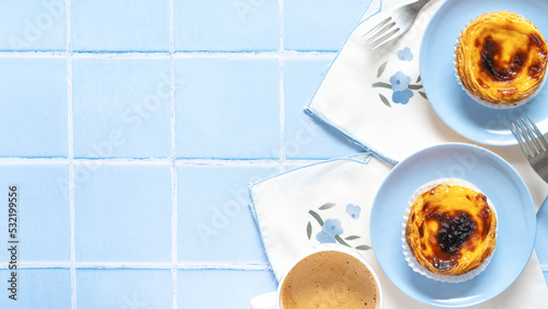 Traditional Portuguese egg tart dessert Pasteis Pastel de nata or Pastels de Belem with a cup of coffee on the blue tile. Flat lay with copy space