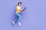 Full length photo of overjoyed pretty person jumping running use netbook isolated on violet color background