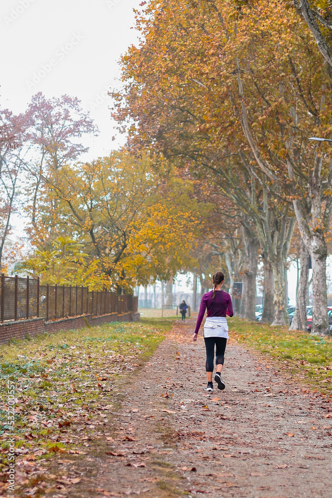 Fototapeta premium Sport in the autumn park. Woman running jogging on a autumn park path. Mock up and copy space.
