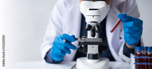 Doctor hand taking a blood sample tube from a rack with machines of analysis in the lab background, Technician holding blood tube test in the research laboratory.