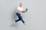 Full length body size view of attractive cheerful man jumping using laptop isolated over grey pastel color background