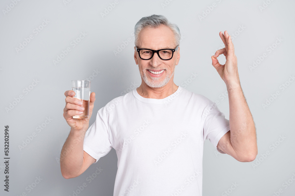 Portrait of cheerful satisfied man hold water glass hand fingers show okey isolated on grey color background Portrait of cheerful satisfied man hold water glass hand fingers show okey isolated on grey color background