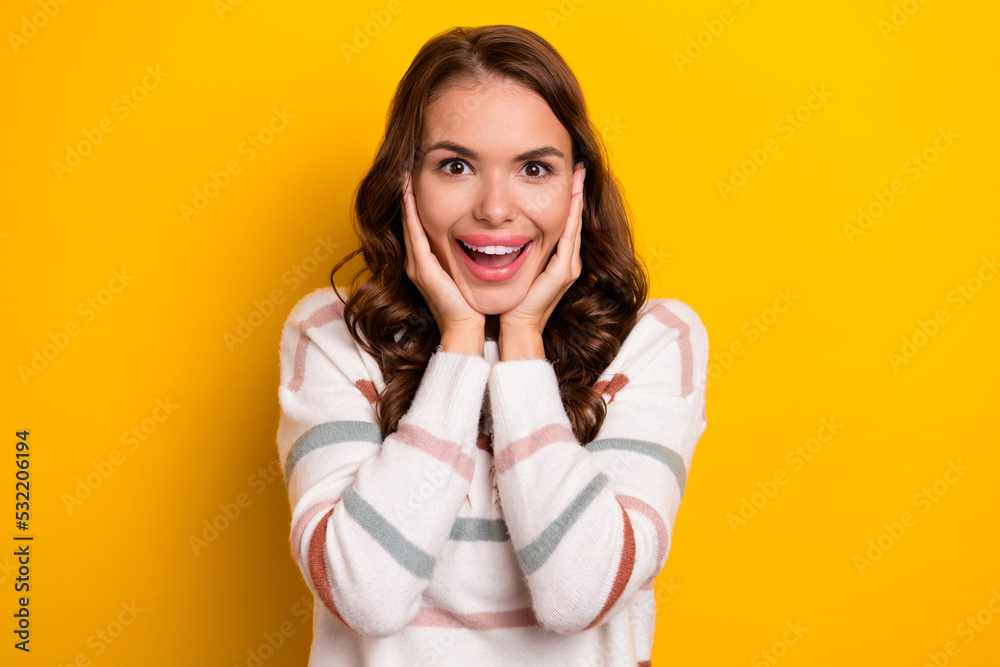 Portrait of lovely impressed girl, hands touch cheekbones toothy smile isolated on yellow color background Portrait of lovely impressed girl, hands touch cheekbones toothy smile isolated on yellow color background