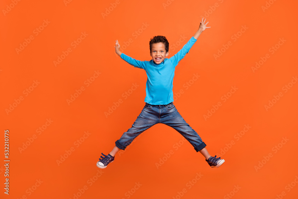 Full size photo of charming little schoolboy jumping high excited back school wear trendy blue garment isolated on orange color background