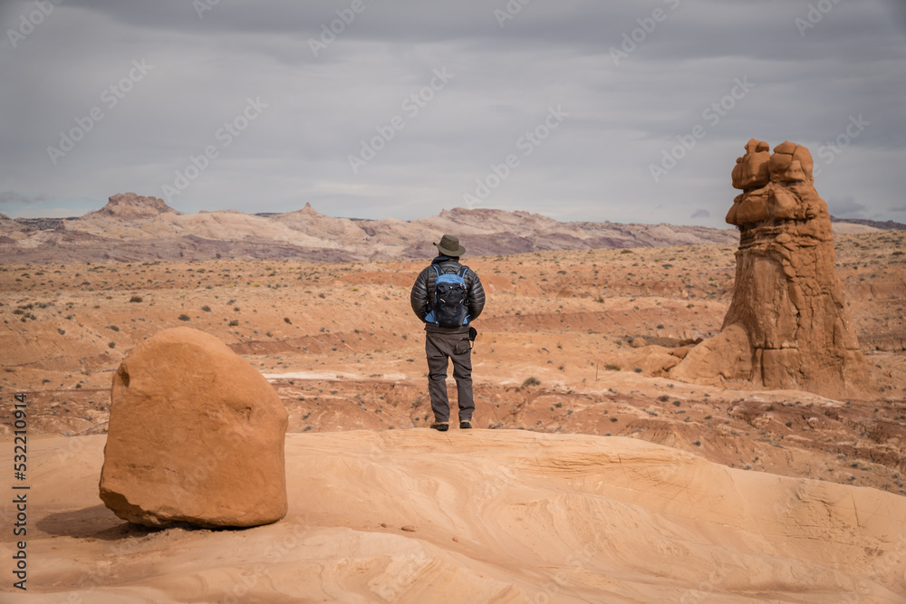 Man hiking among red rock formations in Goblin Valley State Park in Utah.