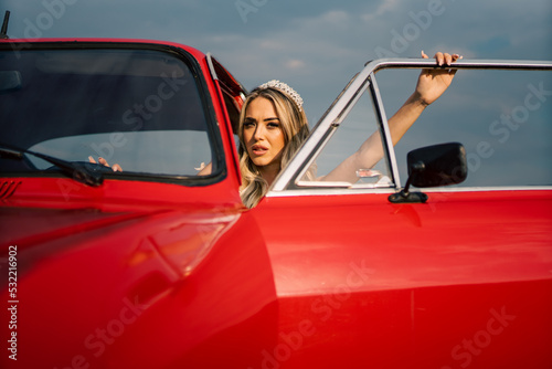 Beautiful bride posing with old vintage red car in sunset.