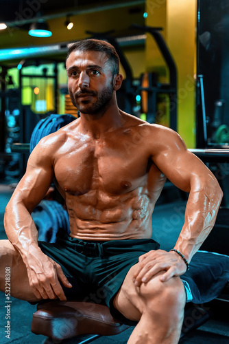 Muscular man posing sitting in gym with lean body.