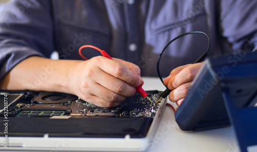 young man who is a computer technician A laptop motherboard repairman is using an IC meter to look for defects on the motherboard to repair on his desk. Board repair with modern technology photo