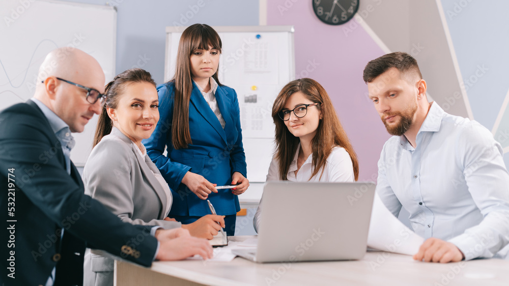 A team of business people are discussing the project together in the office. The team sits at a table and looks at a laptop screen. A team of business people are discussing the project together in the office. The team sits at a table and looks at a laptop screen.