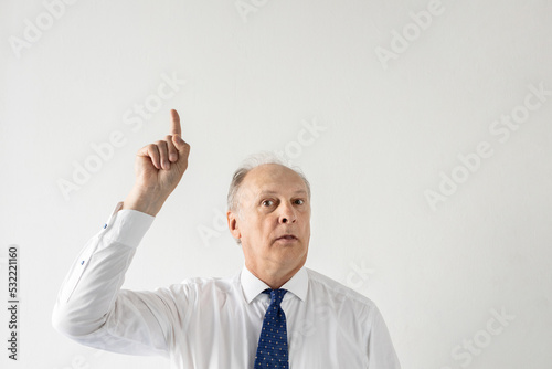 Portrait of confident mature businessman pointing upwards against white background. Senior manager wearing formalwear having idea. Solution and idea concept