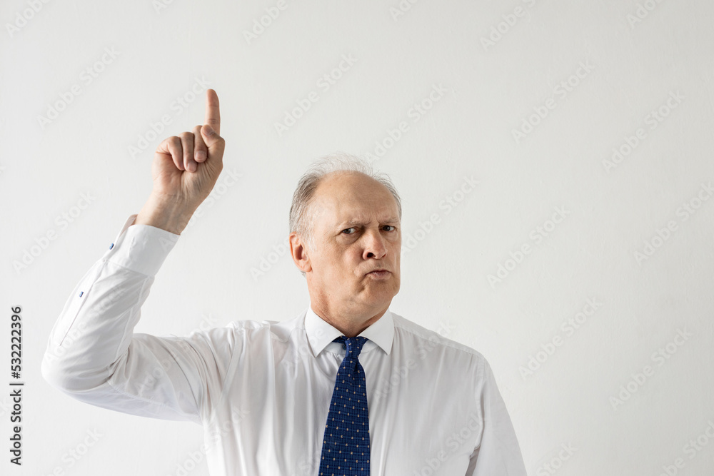 Portrait of frowning mature businessman showing forefinger and looking at camera against white background. Senior manager wearing formalwear having idea. Solution and idea concept Portrait of frowning mature businessman showing forefinger and looking at camera against white background. Senior manager wearing formalwear having idea. Solution and idea concept