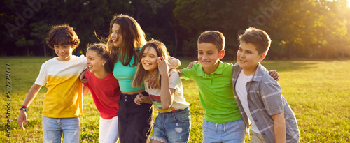Happy kids playing outdoors. Cheerful friends enjoying summer holidays together. Group of children walking on green field, hugging, smiling, and having fun. Banner, header background