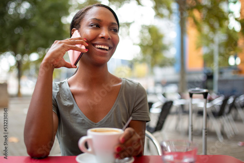 Happy black woman talking on mobile phone at coffee shop