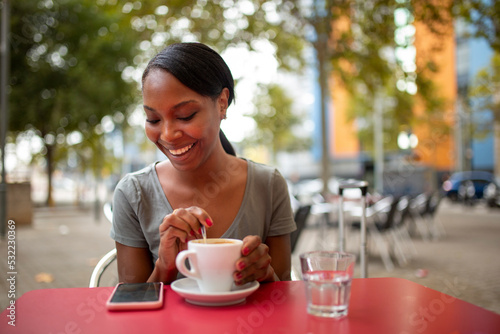 Happy black woman reading text message using mobile phone at coffee shop