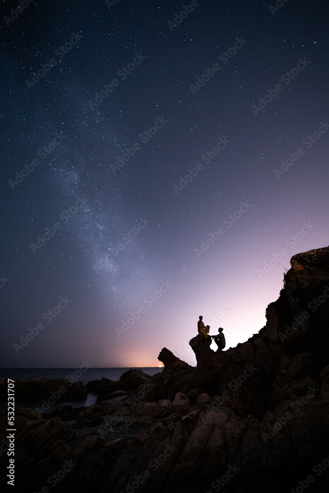 Pareja contemplando la via lactea y el cielo estrellado desde la playa entre rocas