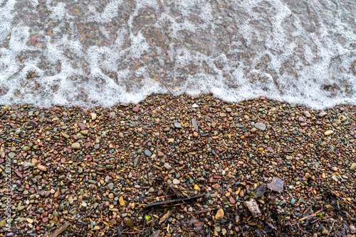 Waves on the rocky shoreline of Lake McDonald in Glacier National Park, with colorful pebbles photo