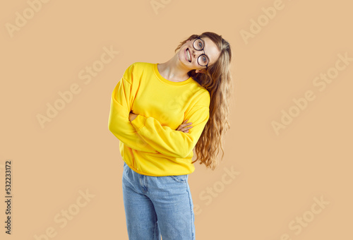 Human emotions. Portrait of cheerful and goofy girl with wide funny and crazy smile on light beige background. Young woman in jeans, sweatshirt and glasses posing with funny grimace on her face.