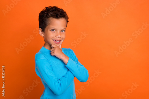 Photo of positive minded boy arm touch face consider dilemma idea plan wear blue pullover empty space isolated on orange color background
