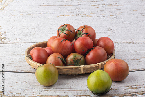 fresh red tomato on wicker basket on gray background.