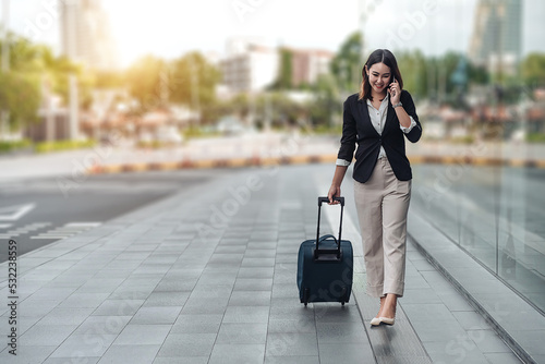 Young Asian businesswoman talking on phone and walking in airport before business trip. Beautiful woman passenger has mobile call and discusses something with smile, holds coffee in hand