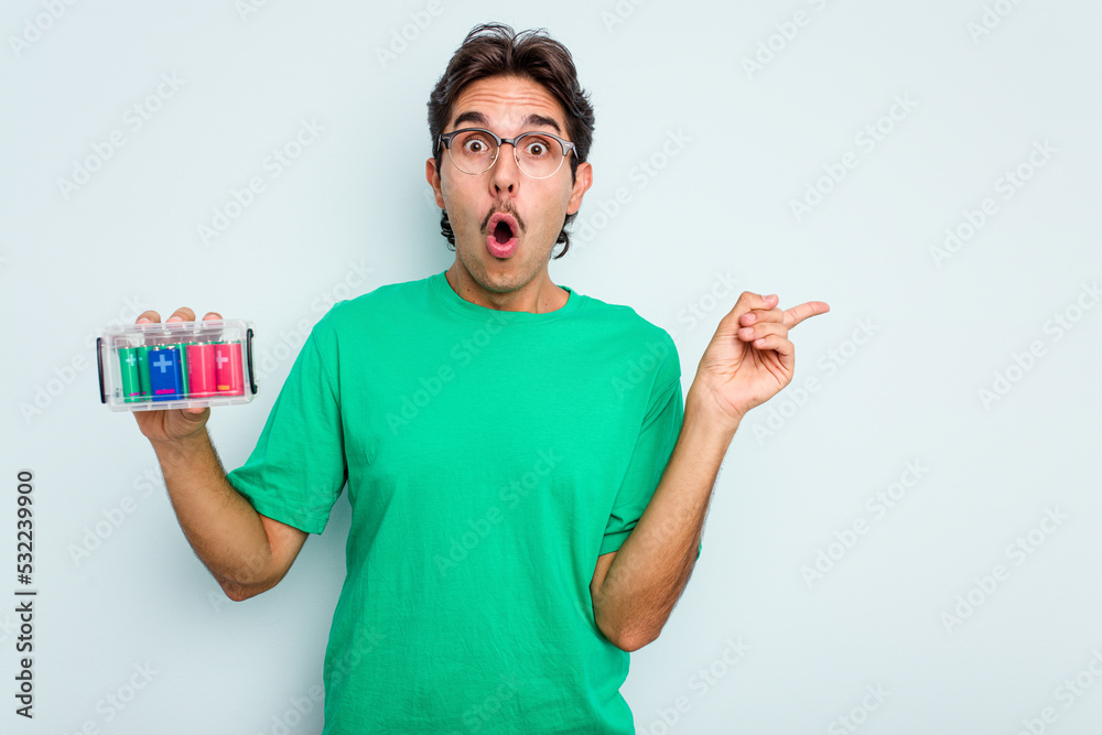 Young hispanic man holding battery box isolated on white background pointing to the side