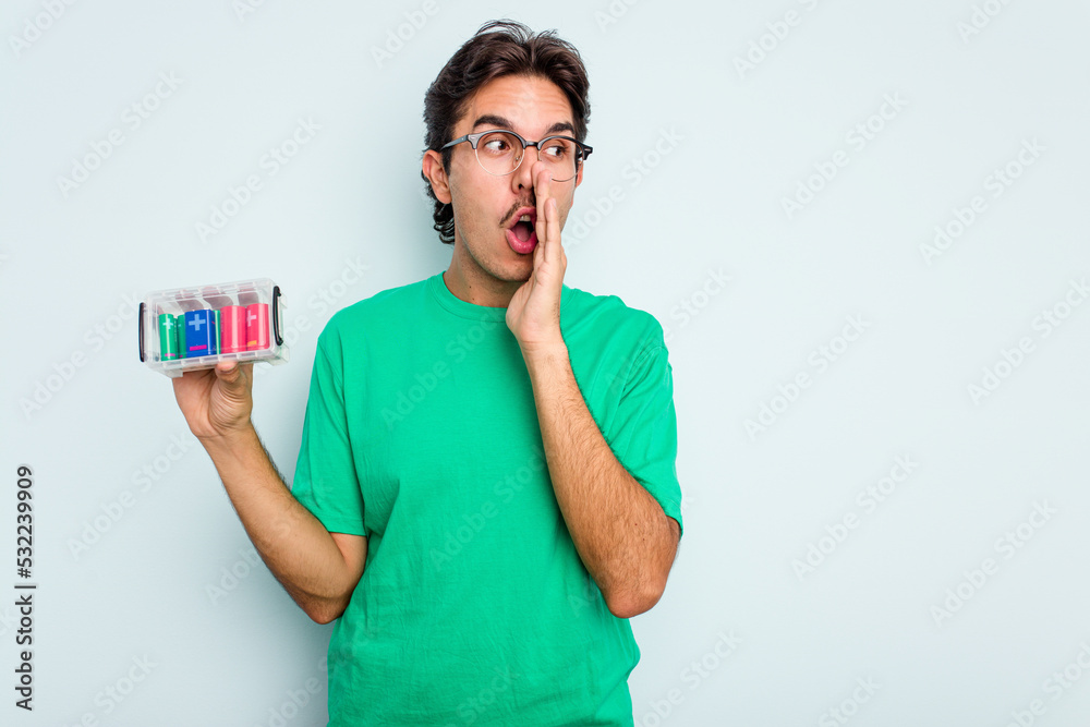 Young hispanic man holding battery box isolated on white background is saying a secret hot braking news and looking aside Young hispanic man holding battery box isolated on white background is saying a secret hot braking news and looking aside