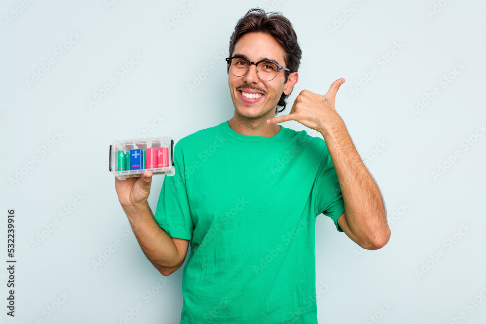 Young hispanic man holding battery box isolated on white background showing a mobile phone call gesture with fingers. Young hispanic man holding battery box isolated on white background showing a mobile phone call gesture with fingers.