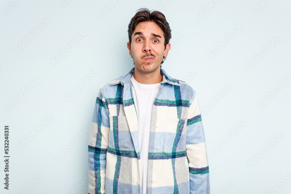 Young hispanic man isolated on blue background blows cheeks, has tired expression. Facial expression concept. Young hispanic man isolated on blue background blows cheeks, has tired expression. Facial expression concept.