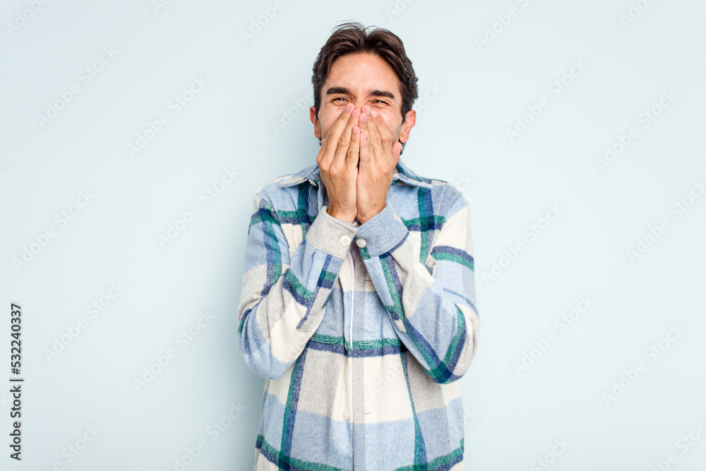 Young hispanic man isolated on blue background laughing about something, covering mouth with hands. Young hispanic man isolated on blue background laughing about something, covering mouth with hands.