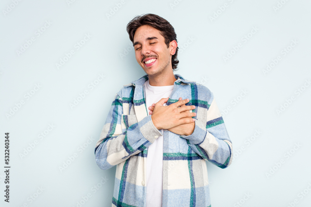 Young hispanic man isolated on blue background laughing keeping hands on heart, concept of happiness. Young hispanic man isolated on blue background laughing keeping hands on heart, concept of happiness.