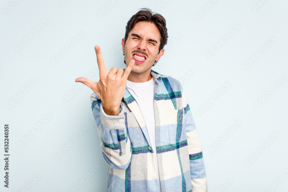 Young hispanic man isolated on blue background showing rock gesture with fingers Young hispanic man isolated on blue background showing rock gesture with fingers