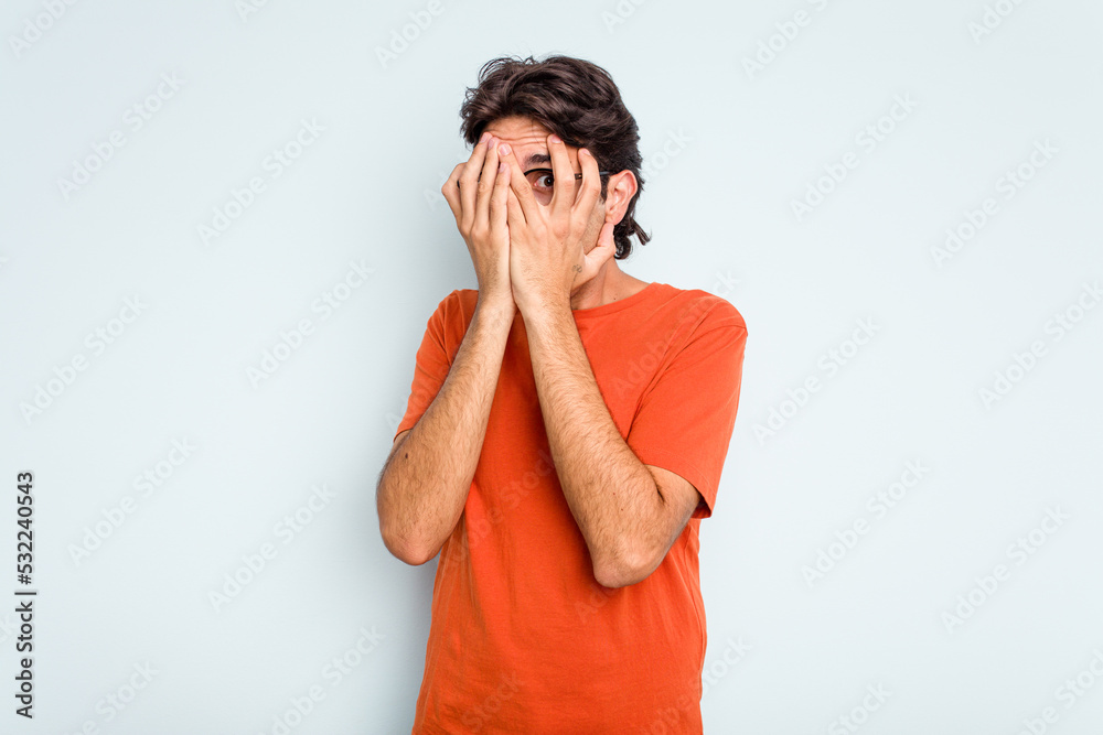 Young hispanic man isolated on blue background blink through fingers frightened and nervous. Young hispanic man isolated on blue background blink through fingers frightened and nervous.