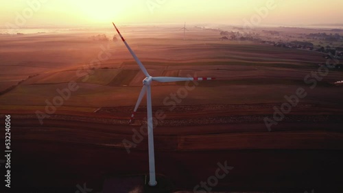 Huge wind trubine with fields in the background and colorful sunrise sky with foggy backgound. Modern environmentally friendly technology. Horizontal shot. High quality 4k footage photo