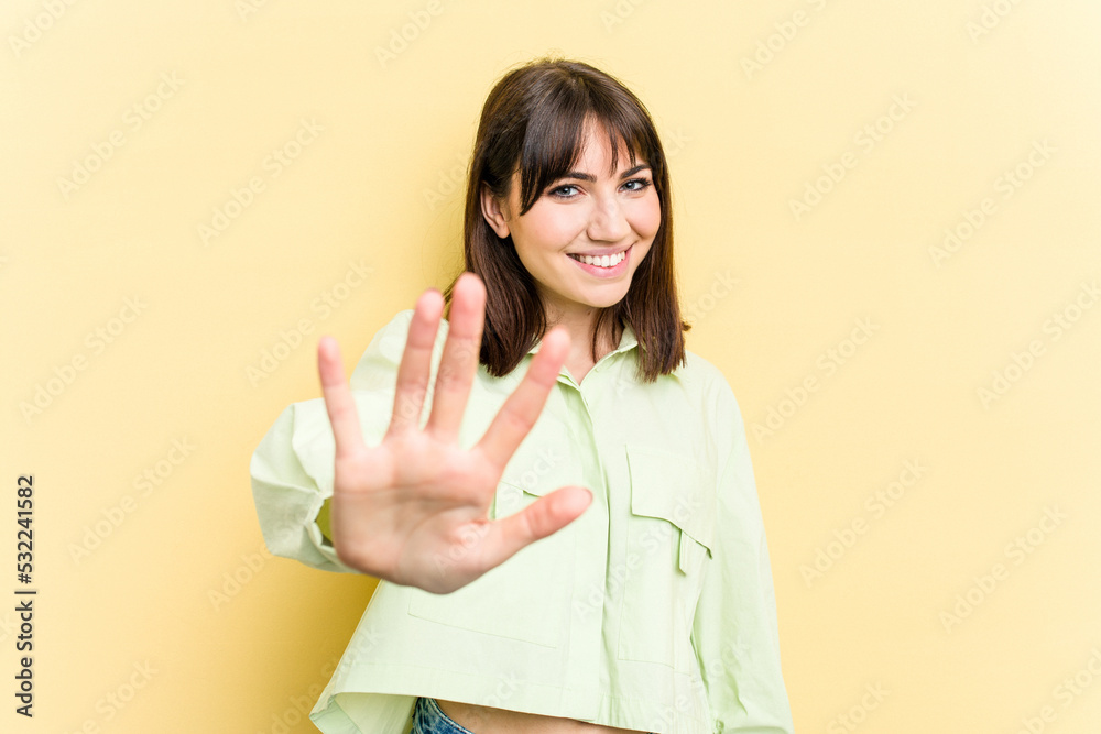 Young caucasian woman isolated on yellow background smiling cheerful showing number five with fingers. Young caucasian woman isolated on yellow background smiling cheerful showing number five with fingers.