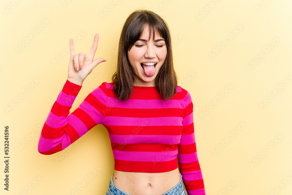 Young caucasian woman isolated on yellow background showing rock gesture with fingers Young caucasian woman isolated on yellow background showing rock gesture with fingers