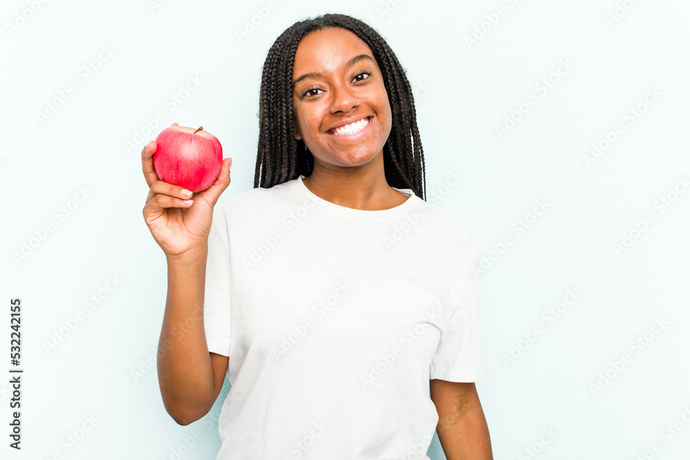 Young African American woman holding an apple isolated on blue background happy, smiling and cheerful. Young African American woman holding an apple isolated on blue background happy, smiling and cheerful.