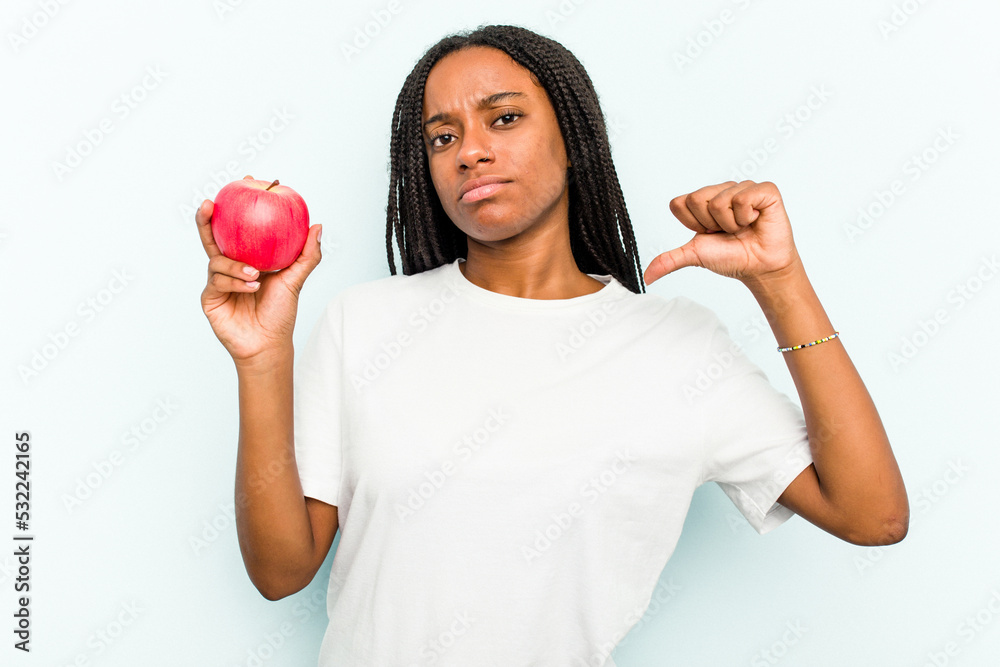 Young African American woman holding an apple isolated on blue background feels proud and self confident, example to follow. Young African American woman holding an apple isolated on blue background feels proud and self confident, example to follow.