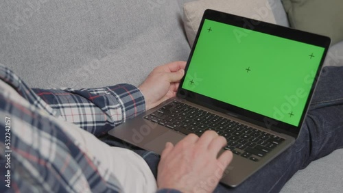Successful middle aged man working from home on laptop with green screen. Creative man sitting on sofa, checking social media, browsing internet. Computer on lap with chroma key