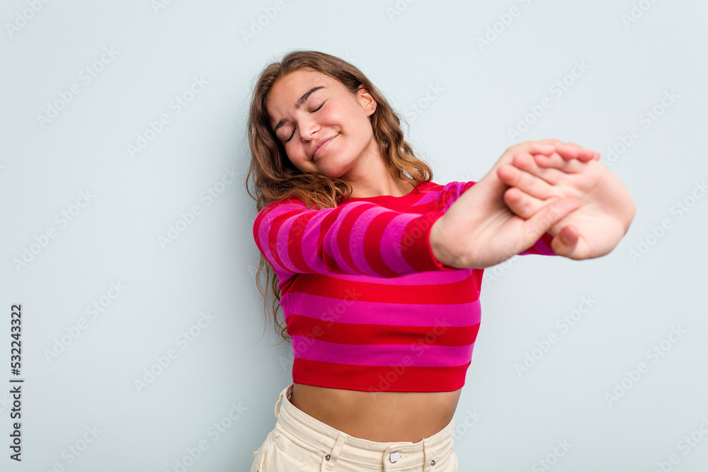 Young caucasian woman isolated on blue background stretching arms, relaxed position.