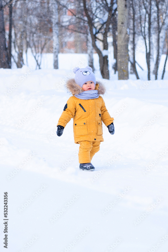 Portrait of toddler 15-20 months old in yellow warm clothes walking in a winter park