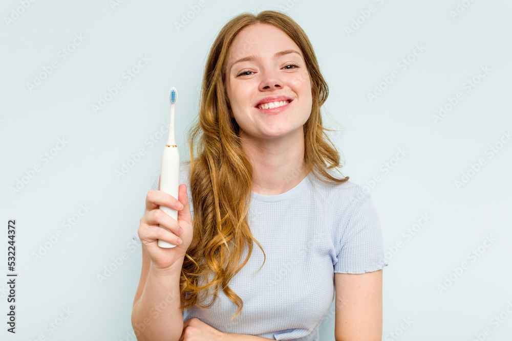 Young caucasian woman holding electric toothbrush isolated on blue background laughing and having fun. Young caucasian woman holding electric toothbrush isolated on blue background laughing and having fun.