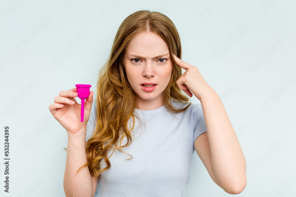 Fototapeta premium Young caucasian woman holding menstrual cup isolated on blue background showing a disappointment gesture with forefinger.