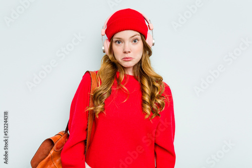 Young student woman wearing headphones isolated on blue background shrugs shoulders and open eyes confused.