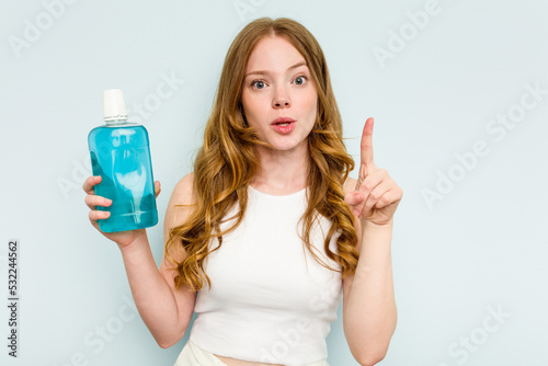 Young caucasian woman holding a mouthwash isolated on blue background having some great idea, concept of creativity.