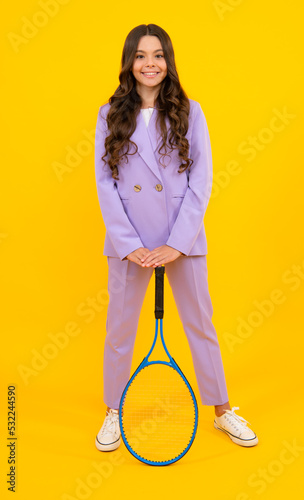 Child tennis player hold tennis racket over isolated yellow background. Sport for kids. Training for teenager girl. © Olena