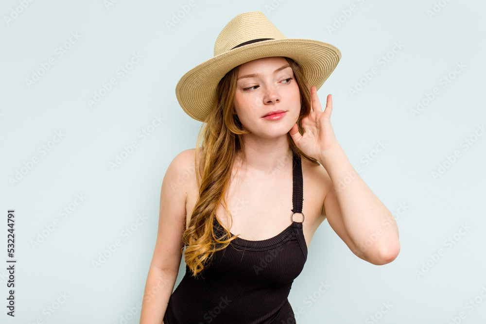 Young caucasian woman going to the beach isolated on blue background trying to listening a gossip. Young caucasian woman going to the beach isolated on blue background trying to listening a gossip.