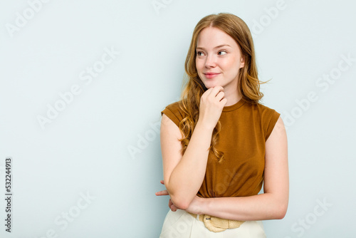 Young caucasian woman isolated on blue background looking sideways with doubtful and skeptical expression.