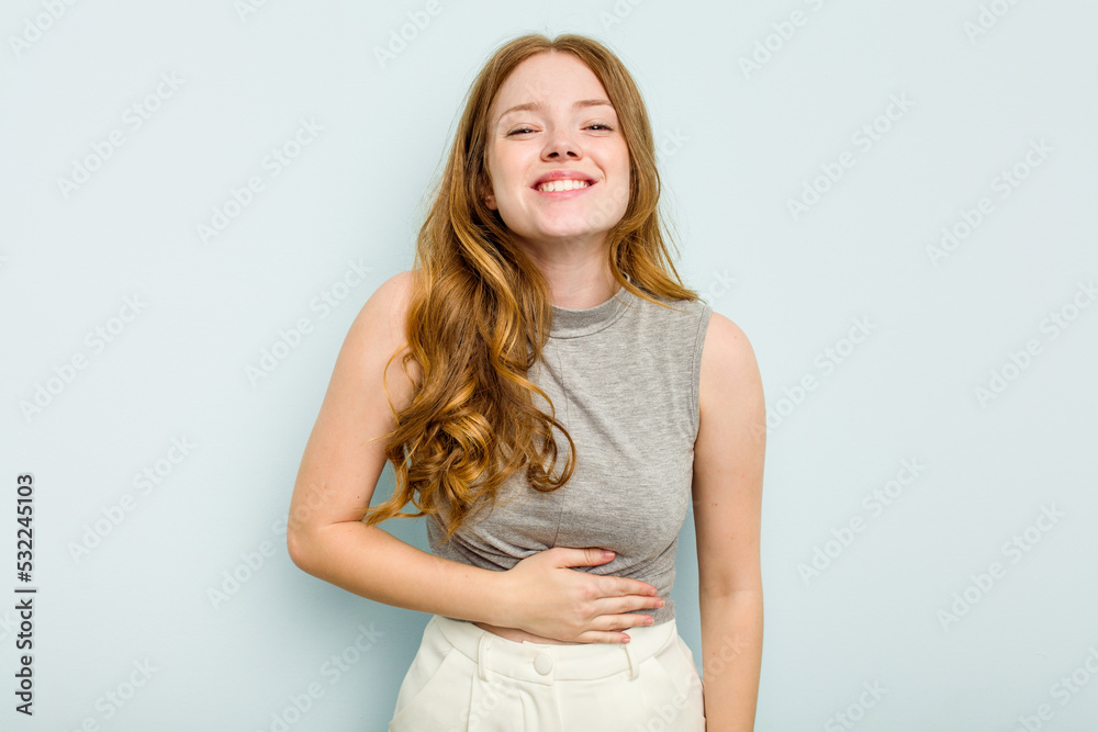 Young caucasian woman isolated on blue background touches tummy, smiles gently, eating and satisfaction concept.