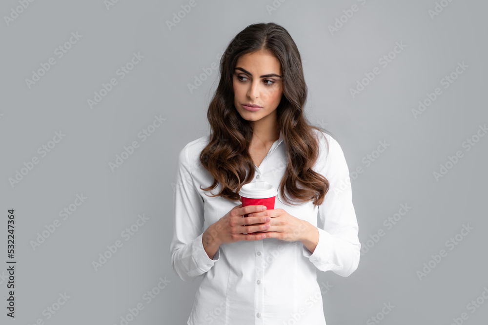 Portrait of a beautiful young woman with a cup of coffee standing on the gray background. Portrait of a beautiful young woman with a cup of coffee standing on the gray background.